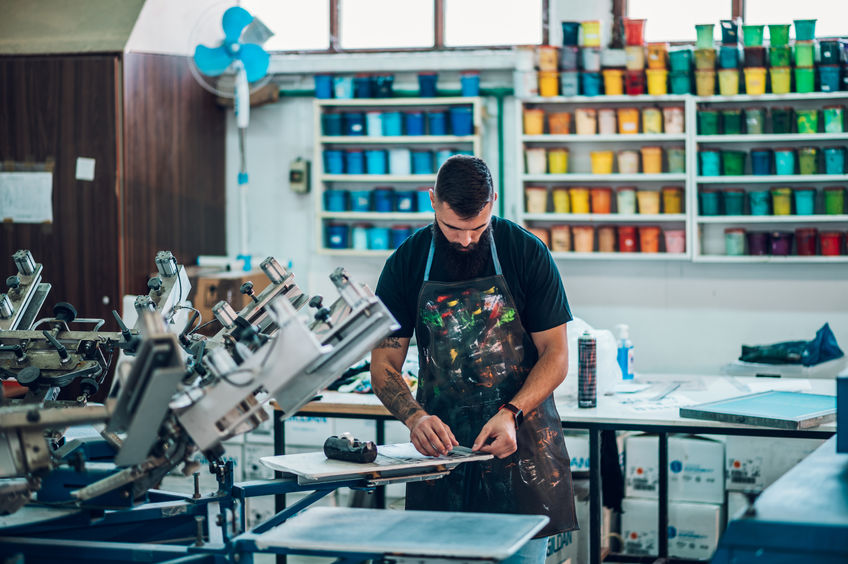 A man in an apron working in an industrial screen printing factory.